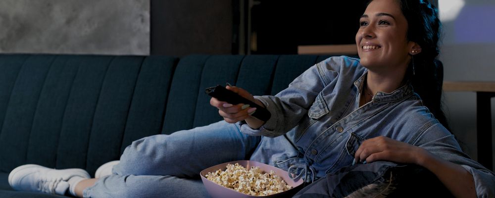 Mulher assistindo os lançamentos da Netflix de junho de 2024 enquanto come pipoca.
